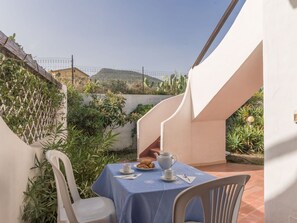 A patio with a table set for two, surrounded by plants and a white chair.