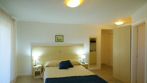 Habitación de hotel con una cama grande, dos mesitas de noche con lámparas, un espejo y una puerta que da a otra habitación.