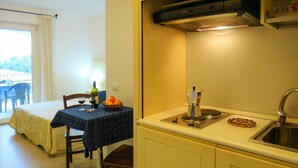 Una pequeña cocina con un lavamanos, una estufa y una mesa con una botella de vino y una cesta de naranjas.
