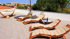 A rooftop terrace with sun loungers, a white umbrella, and a small table with a bottle. - Lovely apartment for 4 people with A/C, TV, terrace and pets allowed (Valledoria)