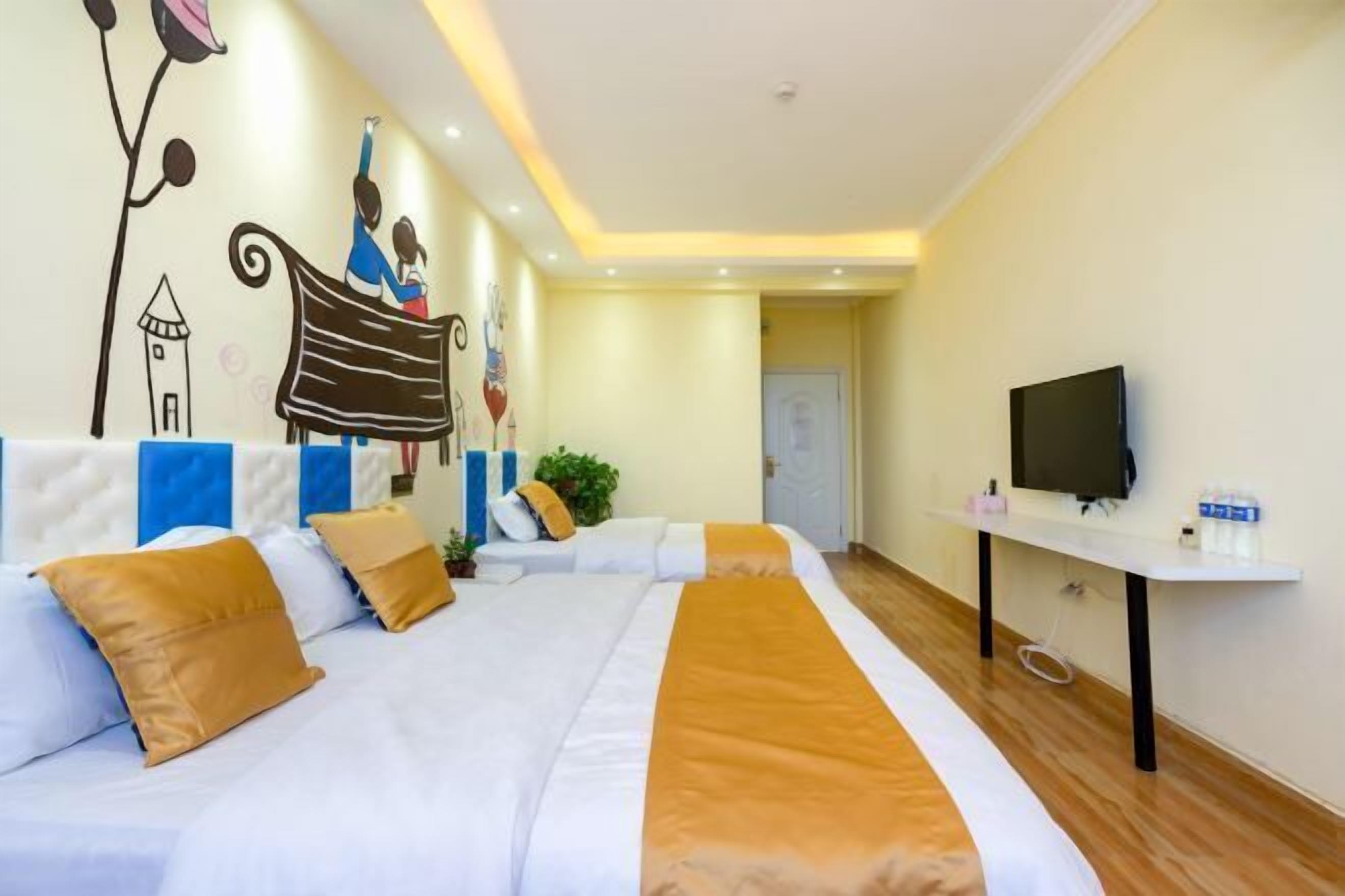 A hotel room with two beds, a TV, a desk, and a mural on the wall.
