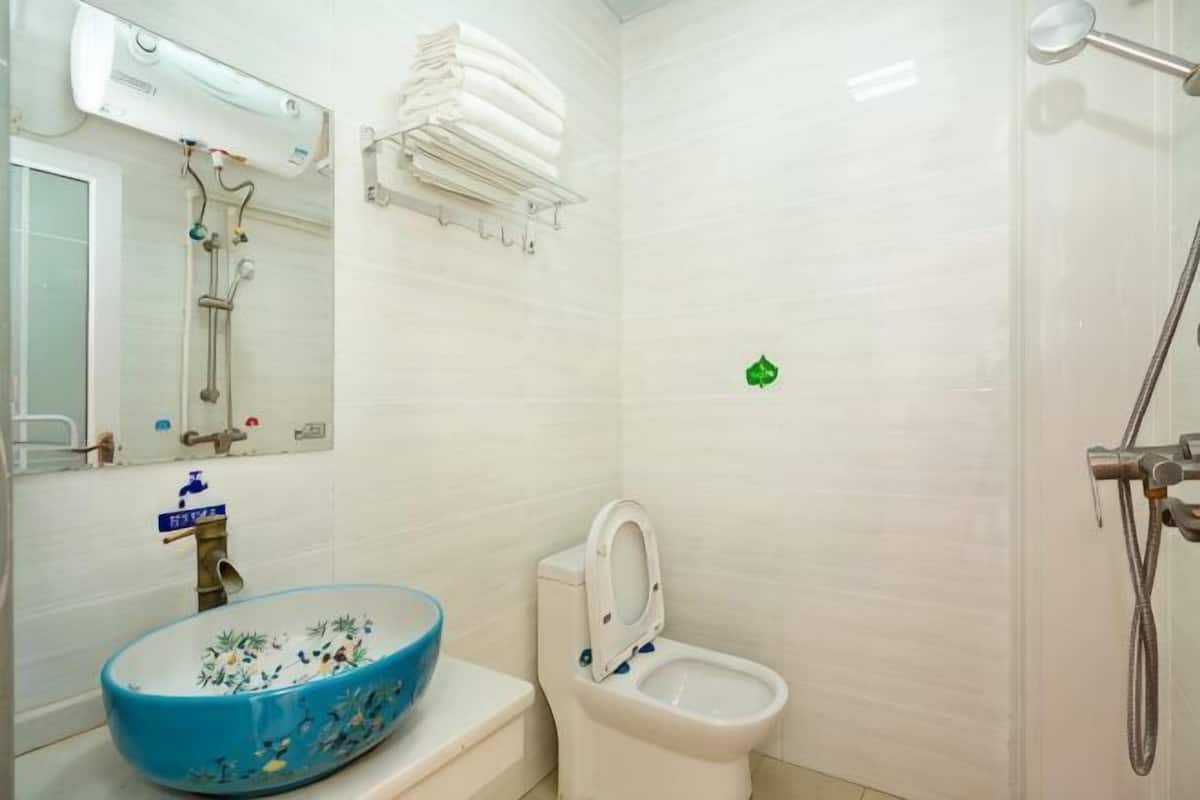 A bathroom with a blue ceramic sink, a toilet, a shower, and a mirror.