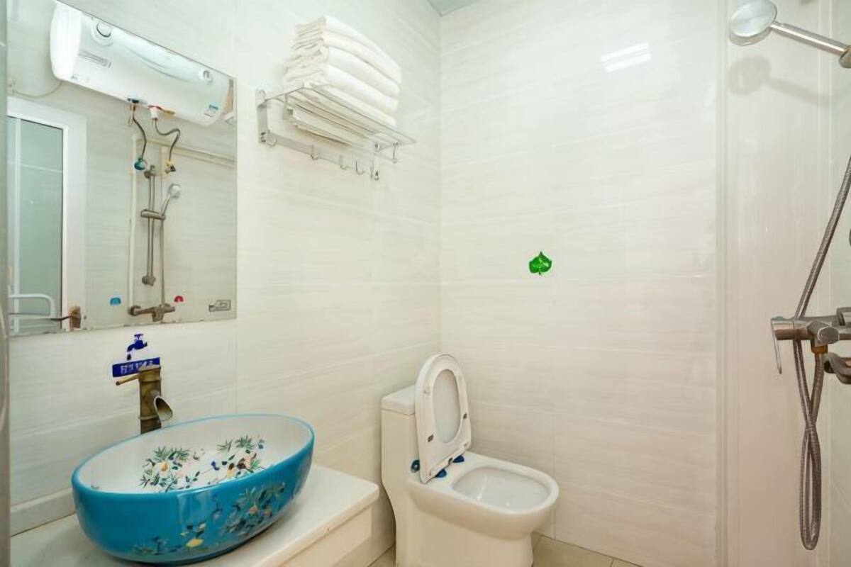 A bathroom with a blue ceramic sink, a toilet, a shower, and a mirror.