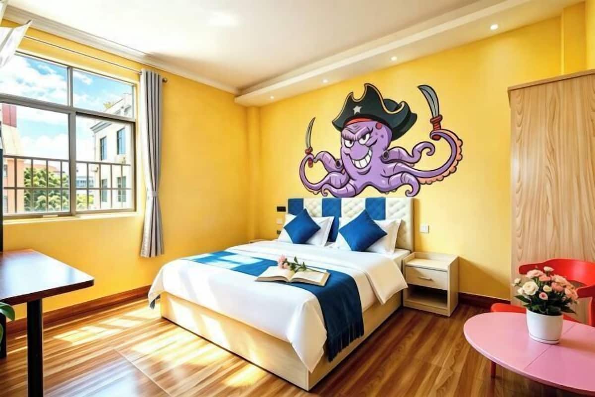 A hotel room with a bed, a nightstand, a window with curtains, a wooden floor, and a wall mural.