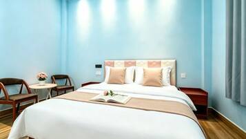 A hotel room with a large bed, a bedside table, a chair, a small round table, and a potted plant.