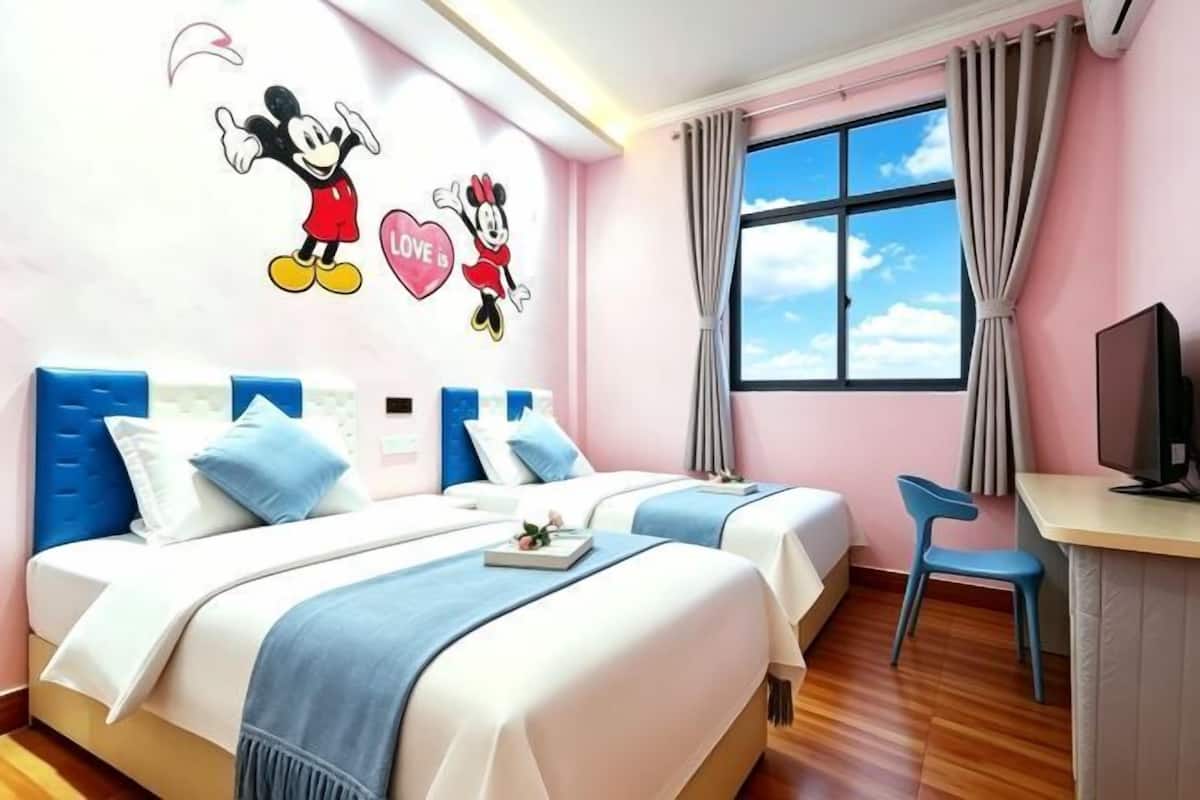 A hotel room with two beds, a desk, a chair, a TV, and a window with curtains.