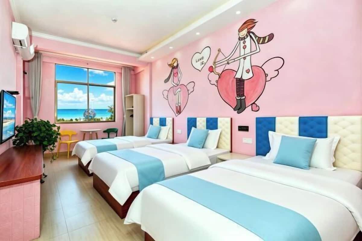 A hotel room with three beds, a TV, a desk, and a window with a view of the ocean.