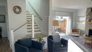 A modern living room with a staircase, two sofas, a small table, and a view of the outside.