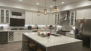 A modern kitchen with white cabinets, a large island with stools, stainless steel appliances, and pendant lighting.