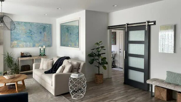 A modern living room with a sofa, coffee table, and decorative items. There is a sliding door and a bench in the background.
