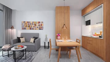Una sala de estar moderna con un sofá gris, una mesa de comedor con sillas, y una zona de cocina con armarios de madera y un microondas.