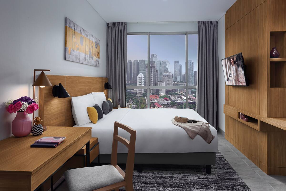 Une chambre d’hôtel moderne dotée d’un grand lit, d’un bureau, d’une chaise, d’une télévision et offrant une vue sur la ville.