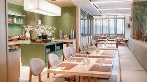 Un espace de restauration moderne avec de longues tables, des chaises et un mur d’accent de couleur verte.