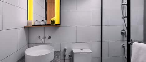 Une salle de bain moderne avec un lavabo rond, des toilettes, une douche et un miroir agrémenté d’une bande lumineuse jaune.