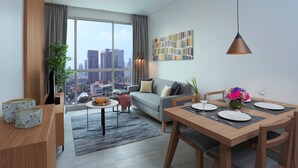Un salon moderne avec une grande fenêtre, un canapé, une table à manger dressée pour quatre personnes et une vue sur la ville.