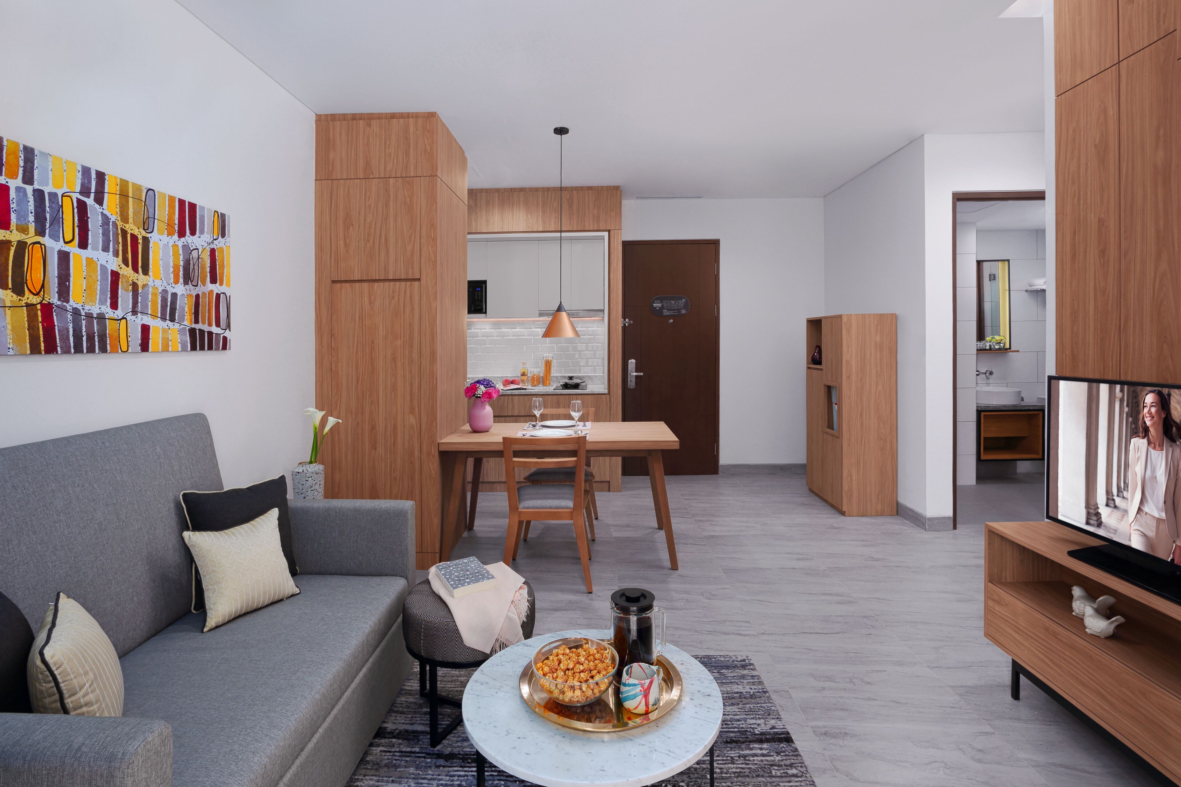 Una sala de estar moderna con un sofá gris, una mesa de comedor y un televisor sobre un mueble de madera.
