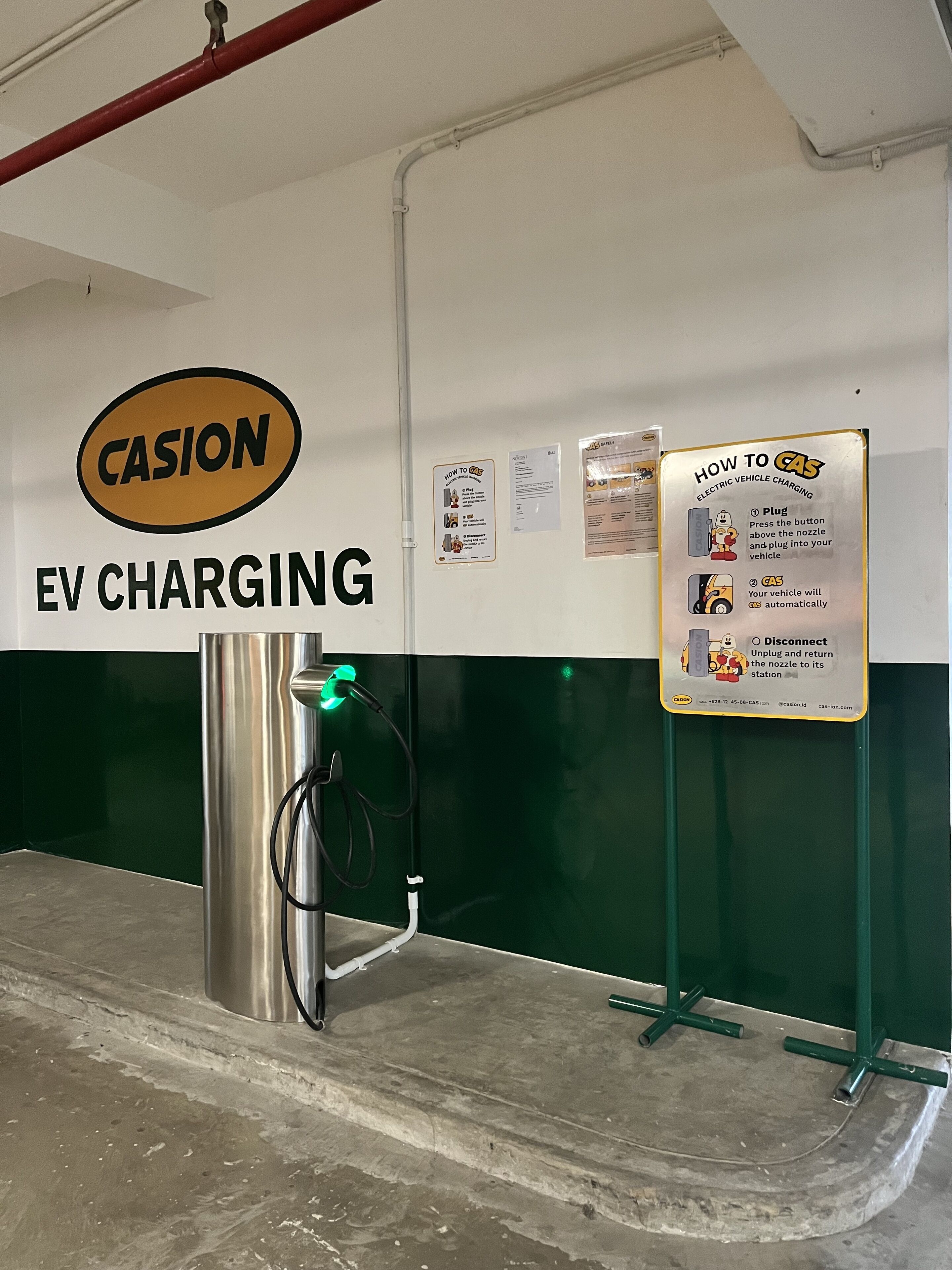 An EV charging station with a Casion sign, charging instructions, and a green wall.