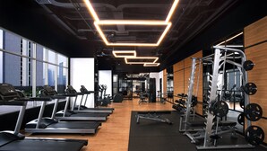 Une salle de sport équipée de tapis de course, d’appareils de musculation et dotée d’une grande fenêtre offrant une vue sur la ville.
