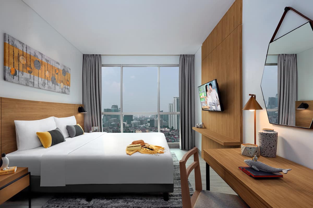 Une chambre d’hôtel moderne dotée d’un grand lit, d’un bureau, d’une télévision et offrant une vue sur la ville.