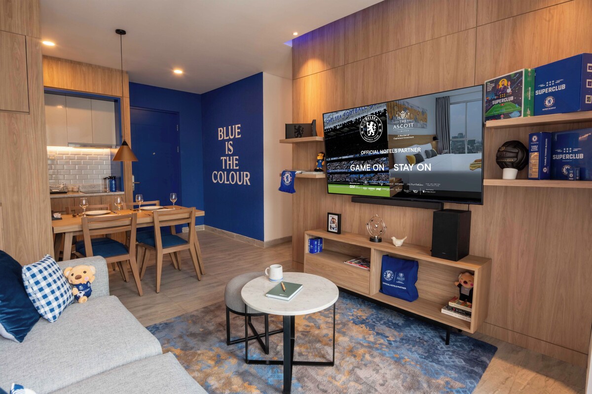 A modern hotel room with a large flat-screen TV, a dining area, a sofa, and a small round table.