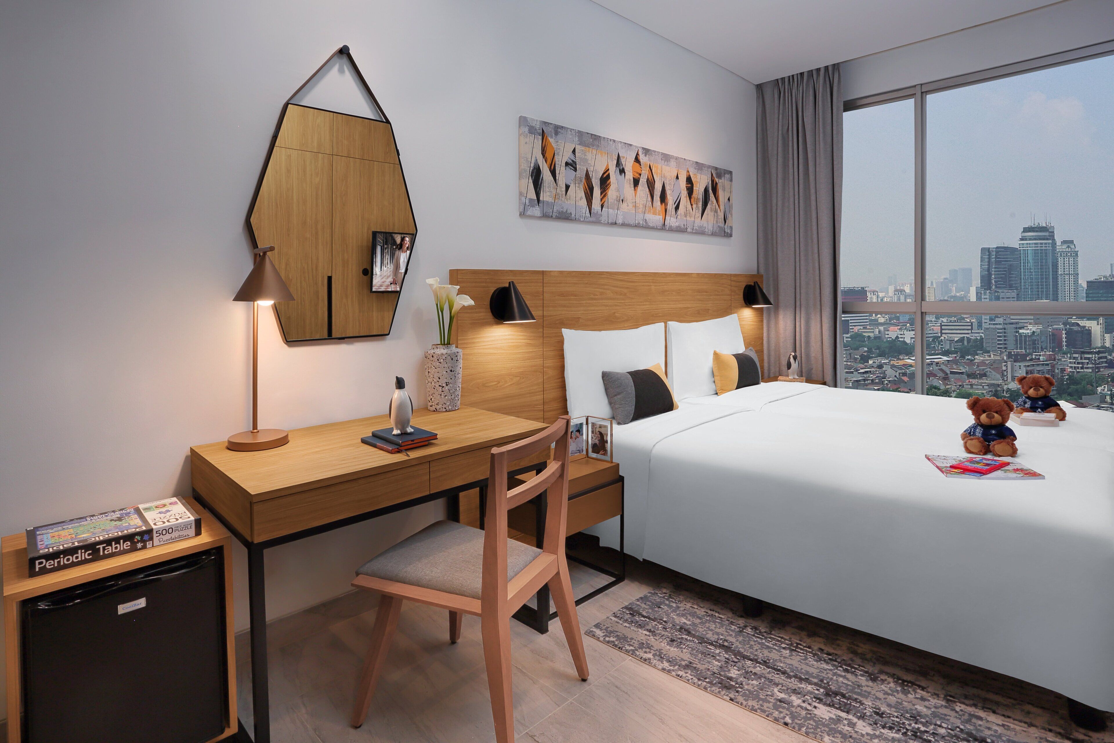 Hotelkamer met een houten bureau, een bed met wit beddengoed, uitzicht op de stad en een schilderij aan de muur.