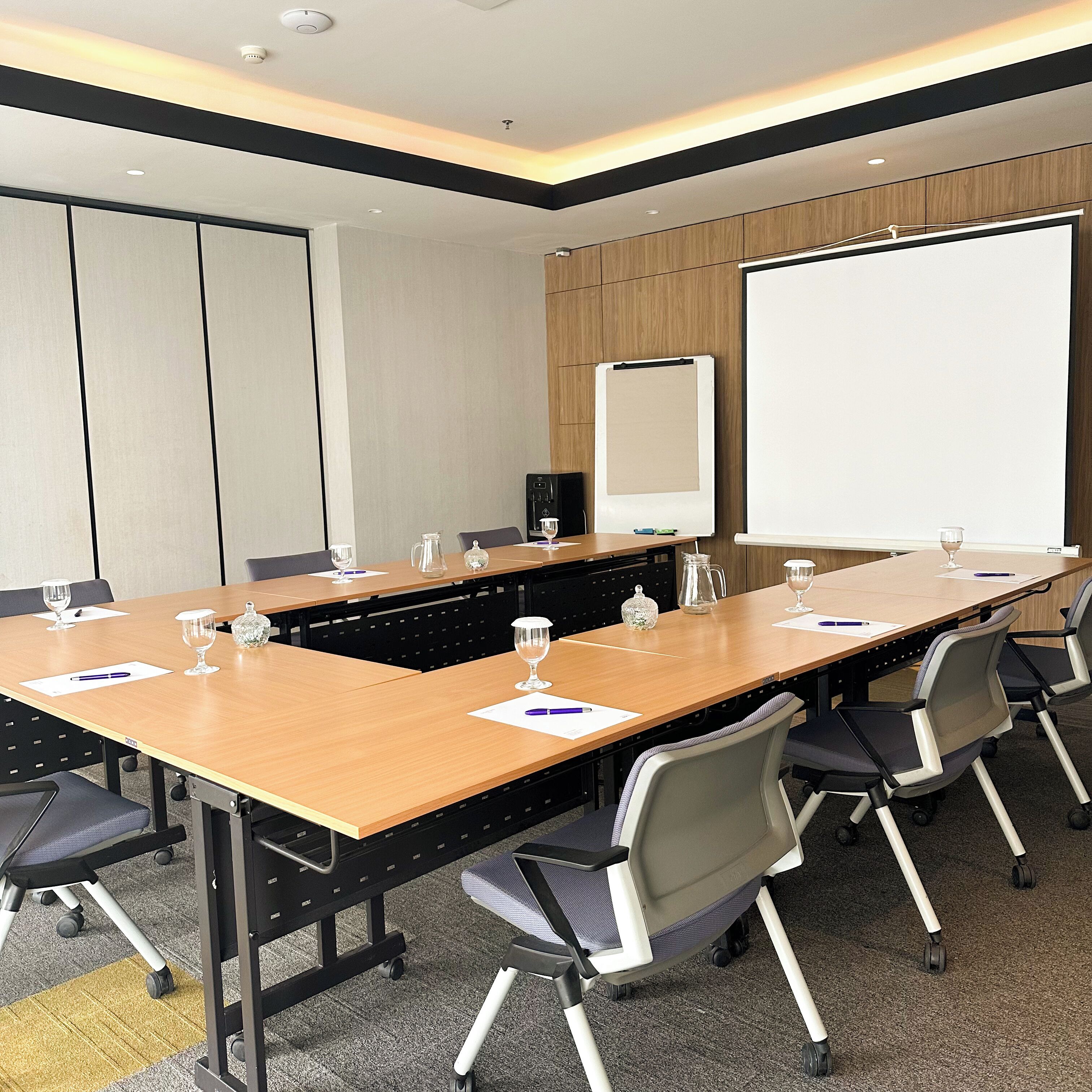 A conference room with a long table, chairs, a whiteboard, and a projector screen.