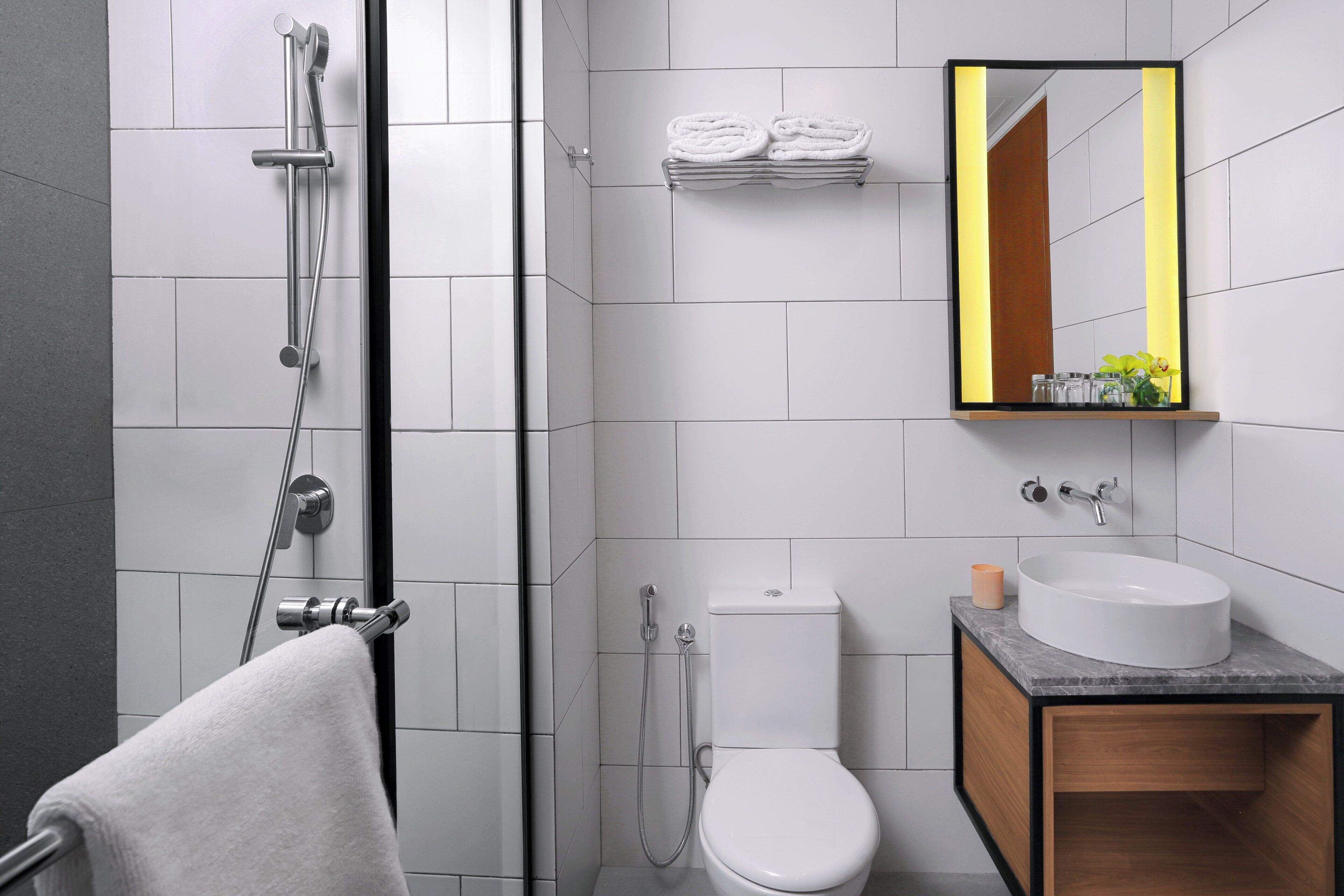 A modern bathroom with a shower, toilet, sink, and a mirror with a yellow frame.