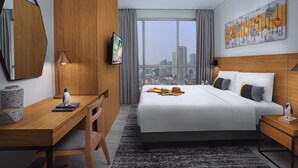 Une chambre d’hôtel moderne dotée d’un grand lit, d’un bureau, d’une chaise, d’une télévision et offrant une vue sur la ville.