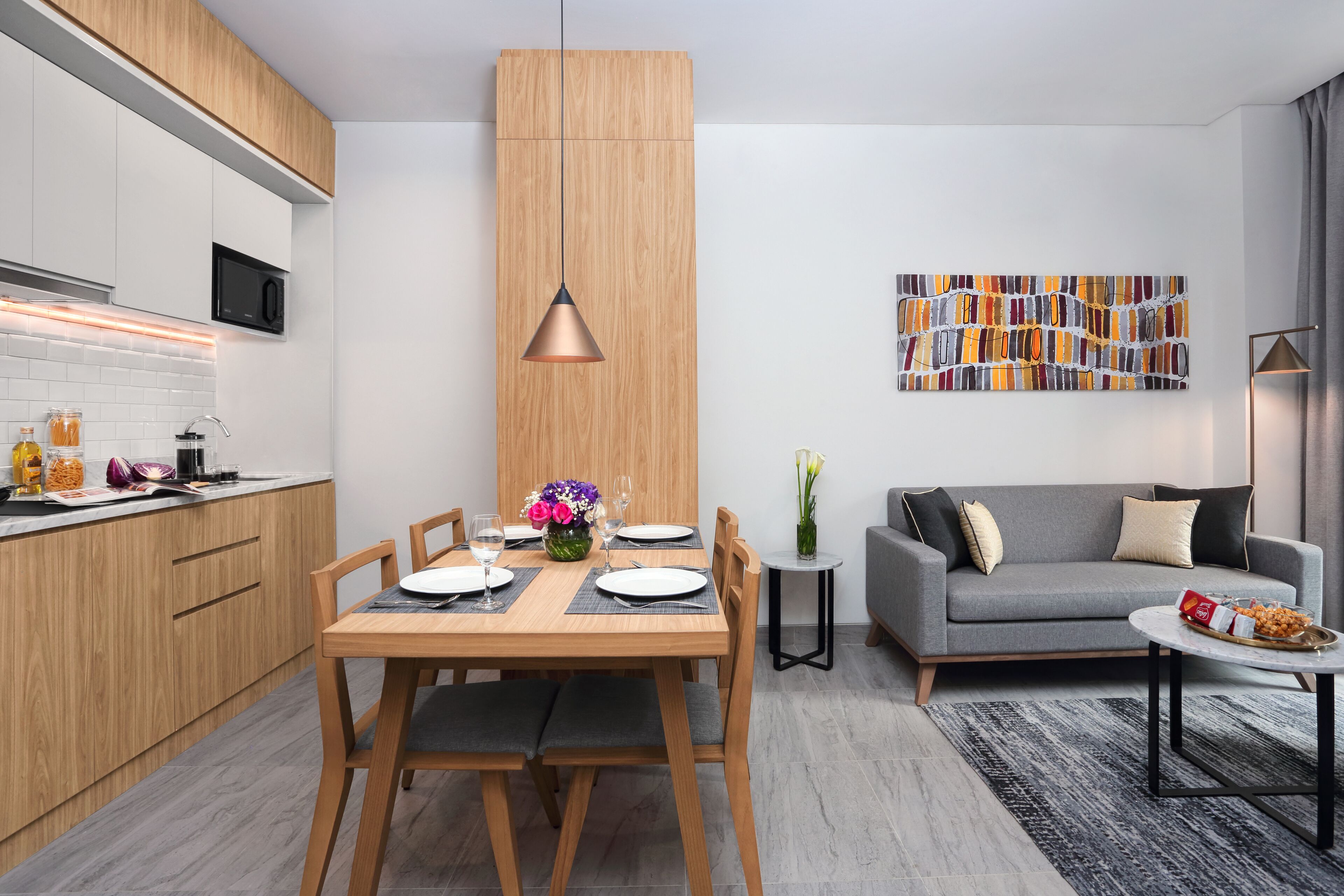 Eine moderne Küche mit Holzausbau, einem Esstisch für vier Personen und einem grauen Sofa im Wohnbereich.