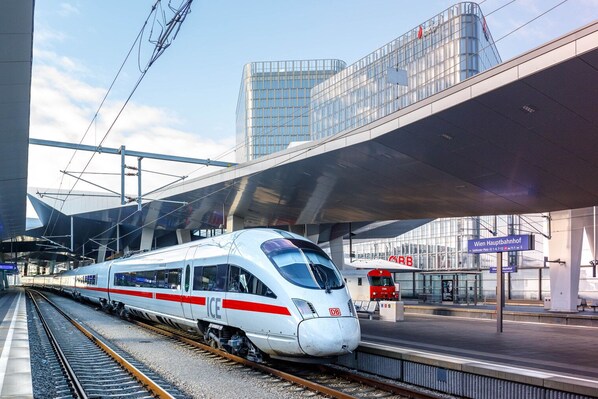 Una estaci ón de tren moderna con un tren de alta velocidad, un andén cubierto y un edificio de cristal al fondo.