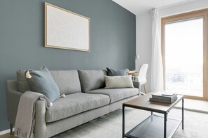 A modern living room with a grey sofa, a coffee table, and a large window with curtains. - Luxe Favoriten 1BR w/ Roof & Bike Storage, close to Park, by Blueground (Vienna)