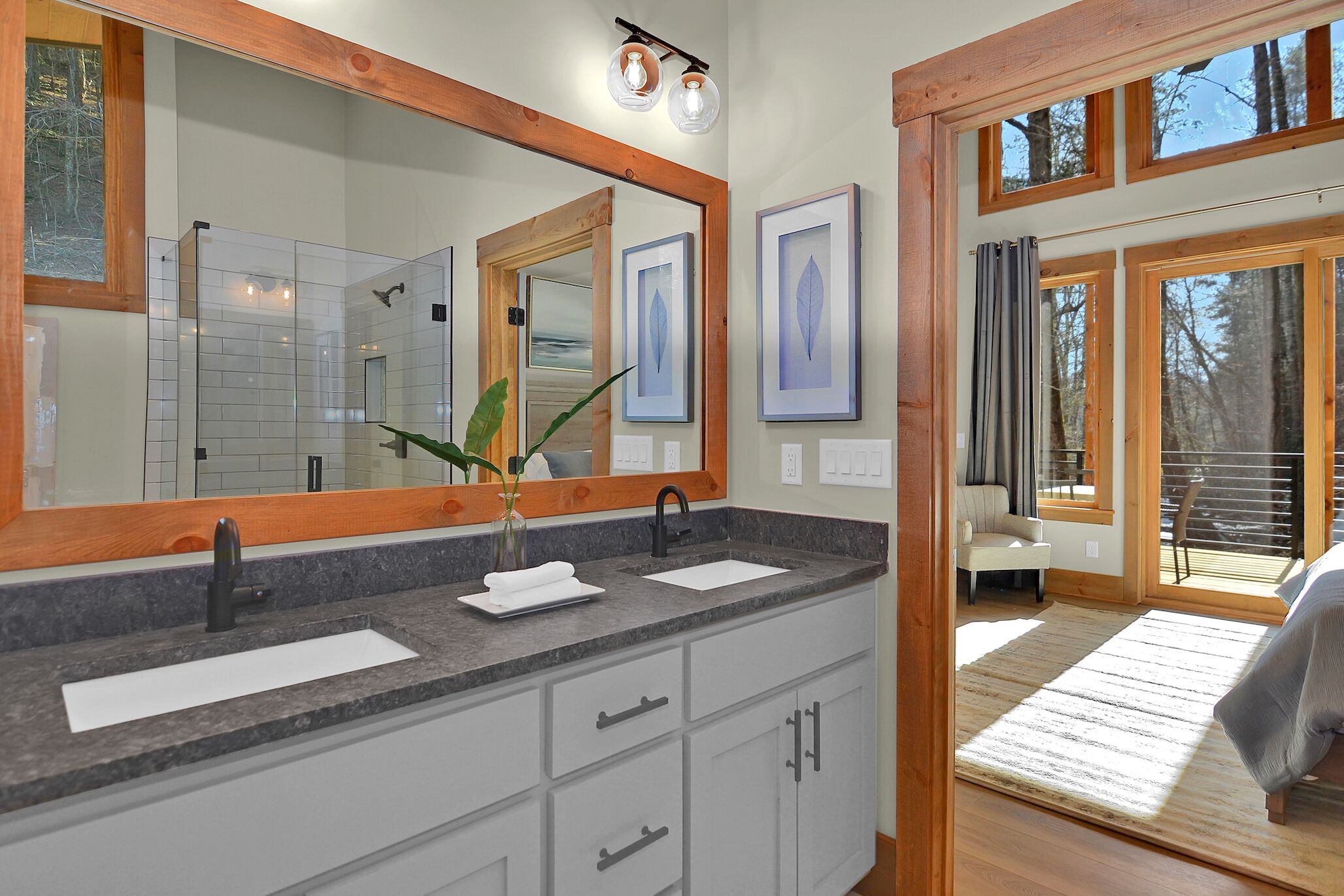 Une salle de bain avec un grand miroir, deux lavabos et une plante.