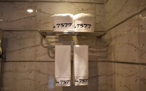 Un baño con paredes de mármol, un perchero con tres toallas y una zona de ducha.