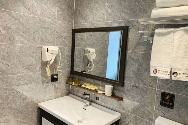A bathroom with a marble wall, a sink, a mirror, a towel rack, and a soap dispenser.