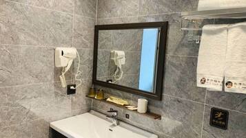 A bathroom with a marble wall, a sink, a mirror, a towel rack, and a soap dispenser.