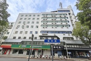 A multi-story building with a modern architectural design, featuring a prominent entrance and signage for a hotel. - Xinjiayuan Hotel (Yizhang)
