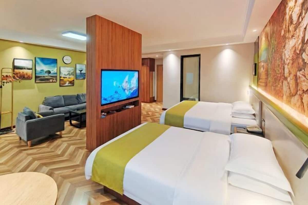 A hotel room with two beds, a TV, a sofa, and a dining table.