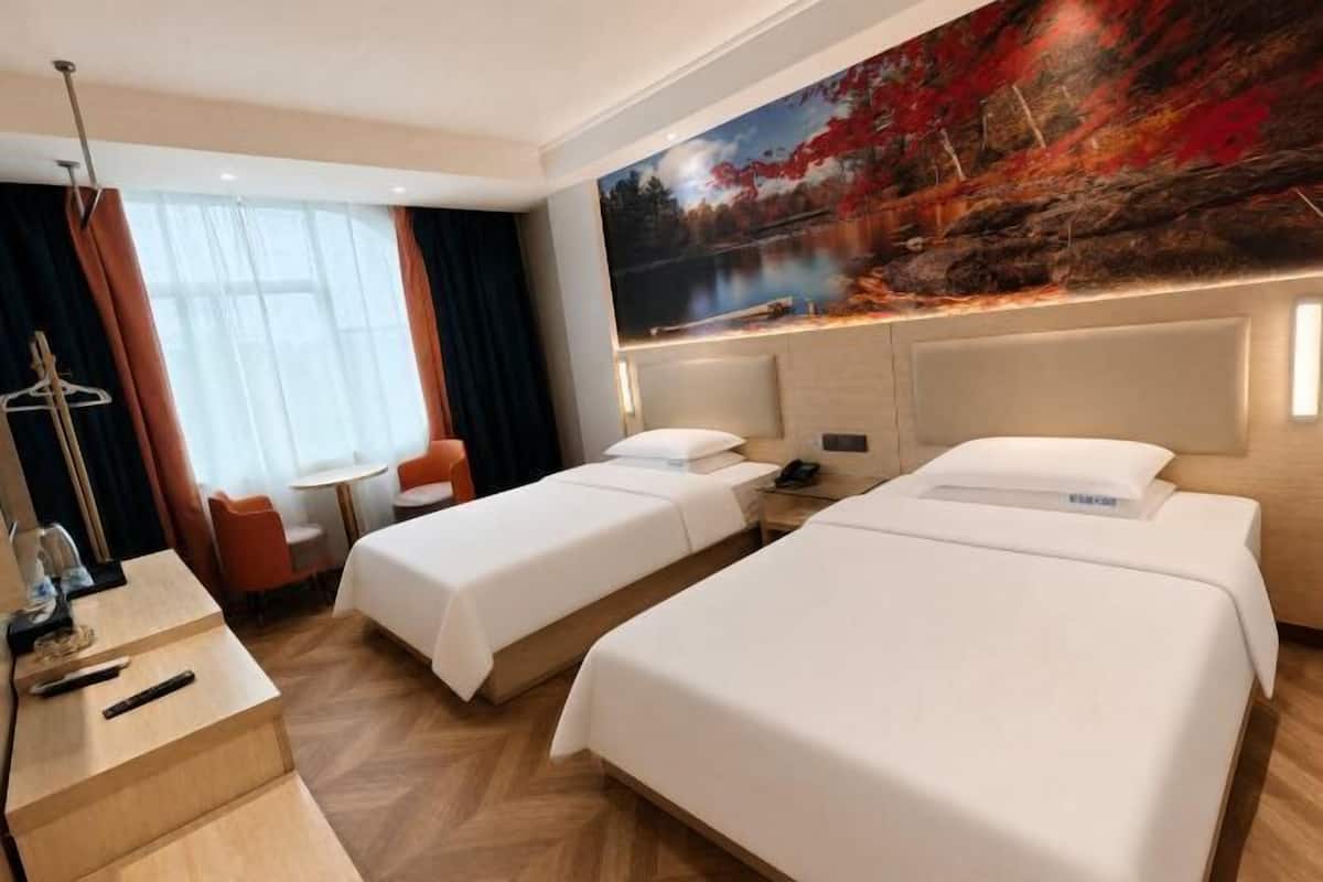 A hotel room with two beds, a desk, a chair, a small table, and a painting on the wall.