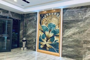 A lobby with a large abstract mural, marble walls, and a glass elevator. - Xinjiayuan Hotel (Yizhang)