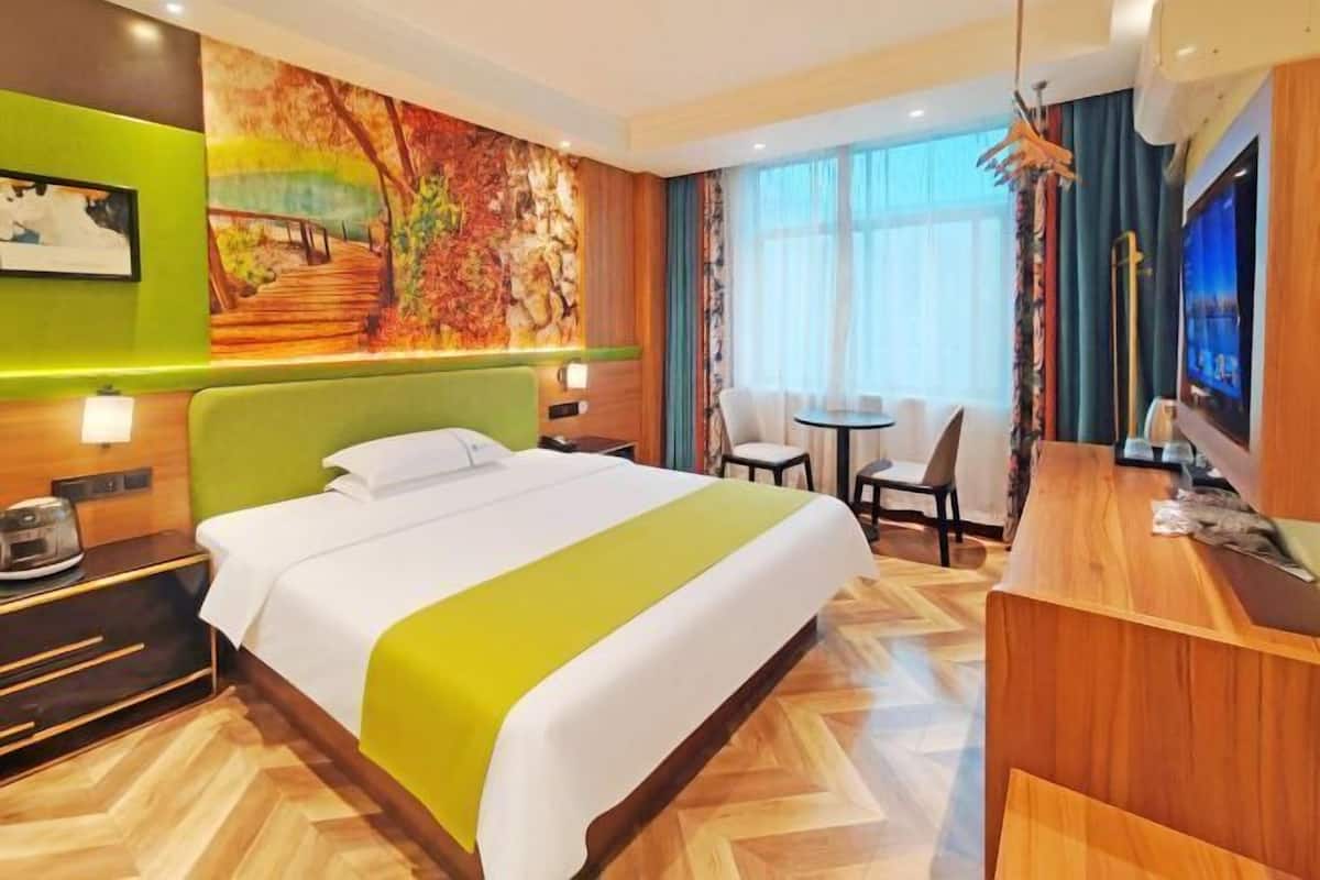 A hotel room with a large bed, a desk, a chair, and a television.