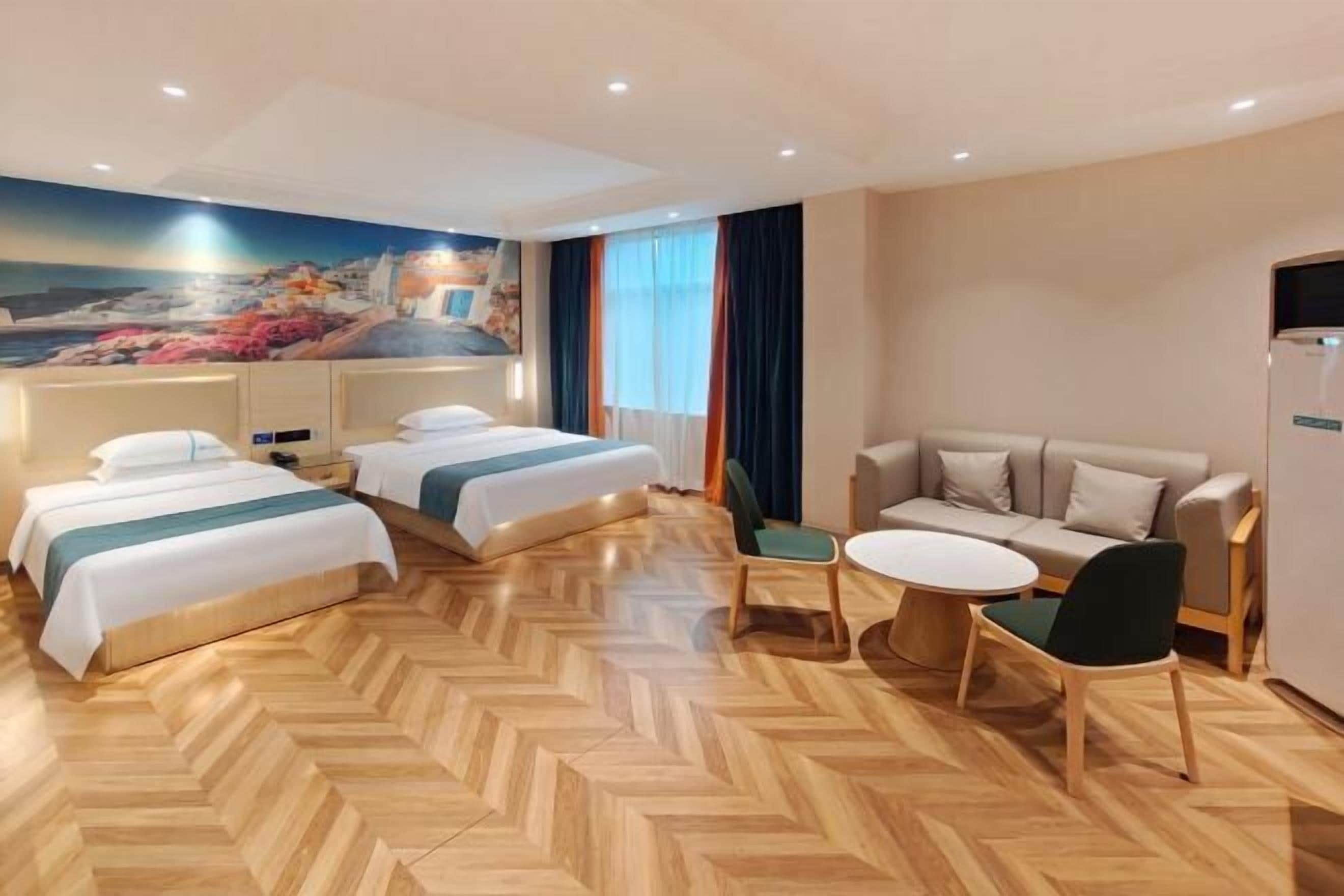 A hotel room with two beds, a sofa, a dining table, and a mural of a coastal scene.
