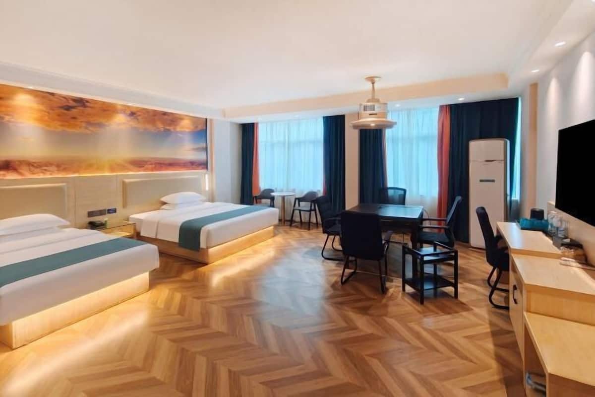 A hotel room with two beds, a desk, chairs, a television, and a large painting on the wall.