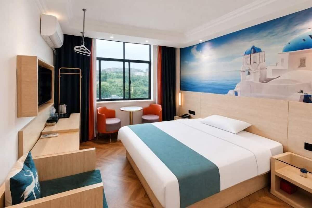 A hotel room with a bed, a desk, a TV, a window with a view, and a painting on the wall.