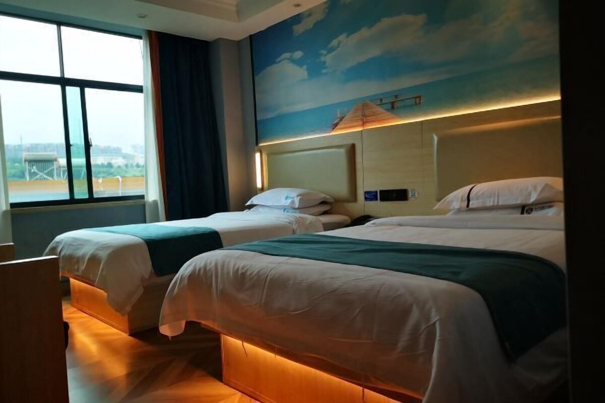 A hotel room with two beds, a large window, and a mural of a beach scene.