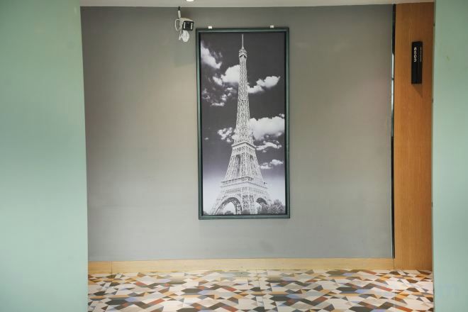 A framed picture of the Eiffel Tower on a wall, a patterned floor, and a door with a sign.