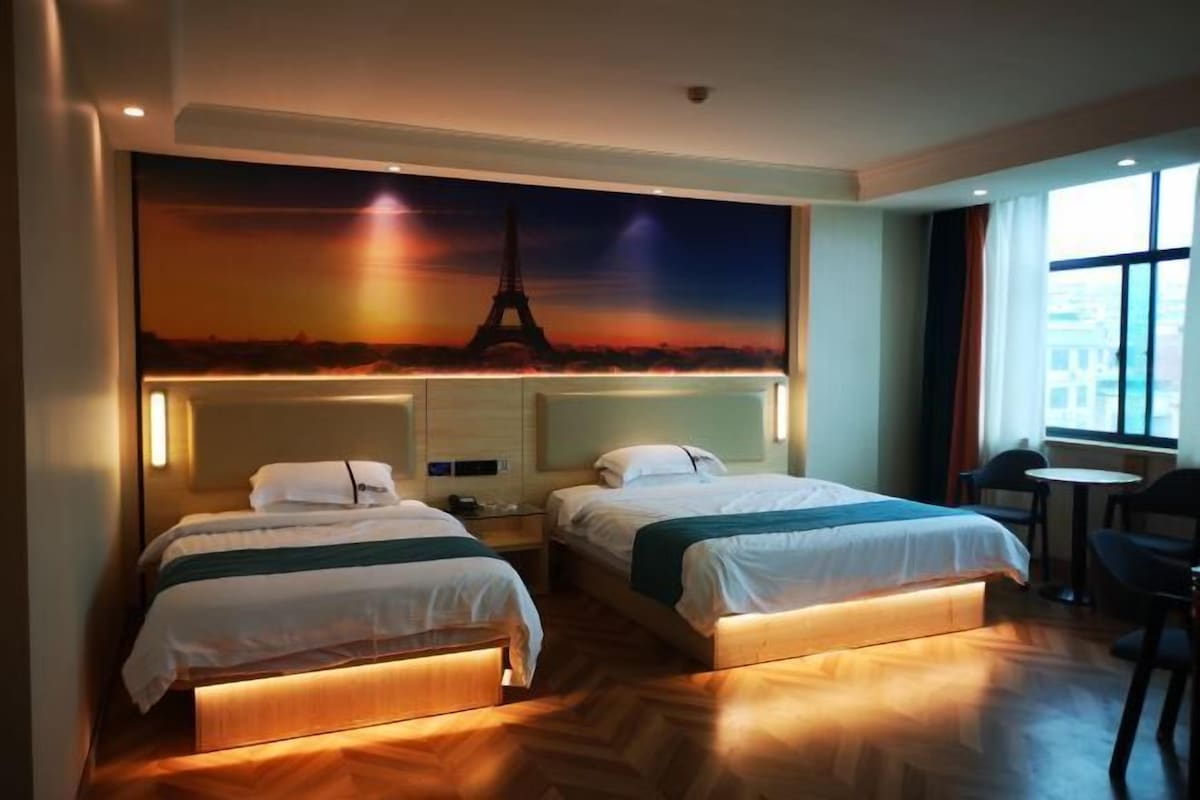 A hotel room with two beds, a large mural of the Eiffel Tower, a small table, and a chair.