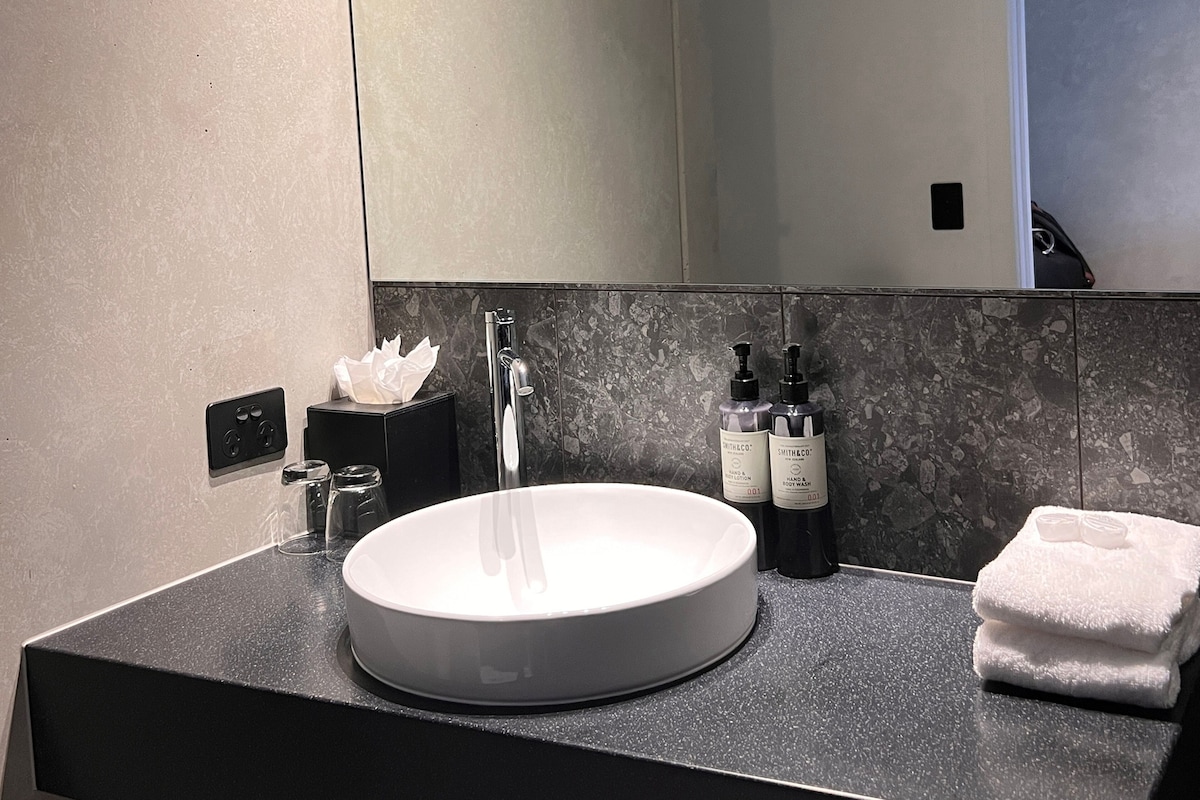 Un baño moderno con un lavabo redondo, un espejo y un perchero para toallas.