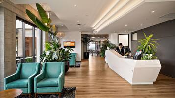 Un área de recepción moderna con suelo de madera, sillas color turquesa y un mostrador blanco.