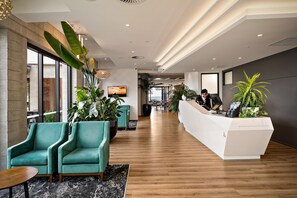 A modern reception area with a wooden floor, teal chairs, and a white reception desk. - Sudima Kaikoura (Kaikoura)