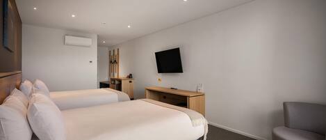 A hotel room with two beds, a desk, a chair, a flat-screen TV, and an air conditioning unit.